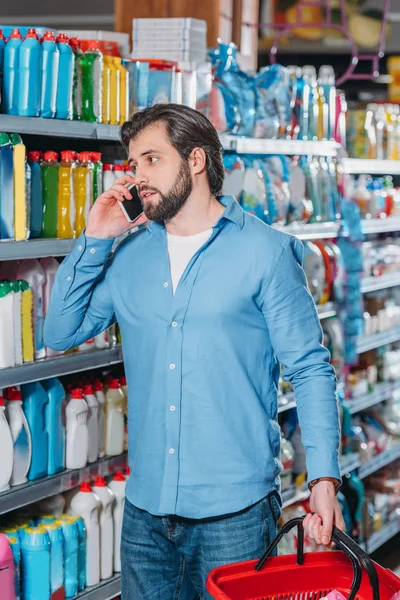 Portrait of man talking on smartphone while choosing detergents in supermarket — Stock Photo