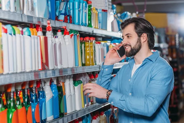 Retrato do homem falando no smartphone ao escolher detergentes no supermercado — Fotografia de Stock