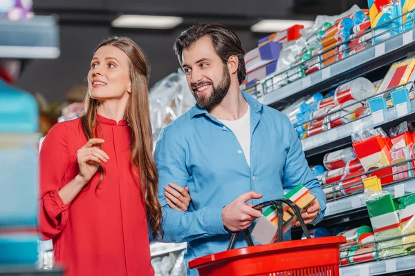 Retrato de casal sorridente com compras cesta compras juntos no supermercado — Fotografia de Stock