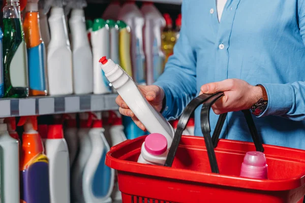 Vista parcial del comprador poniendo detergente en la cesta de la compra en el supermercado - foto de stock