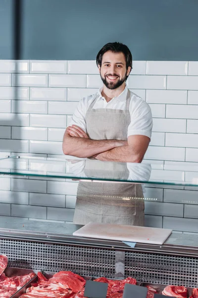 Ritratto di commessa sorridente in grembiule con le braccia incrociate in piedi al bancone del supermercato — Foto stock