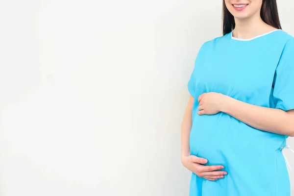 Cropped shot of pregnant woman in medical coat touching her belly on white — Stock Photo