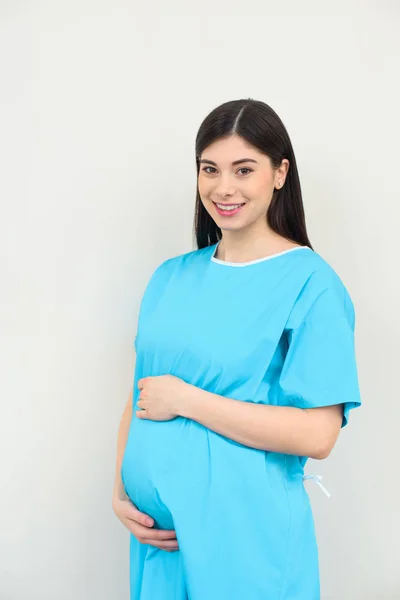 Joven embarazada con abrigo médico tocando su vientre en blanco - foto de stock