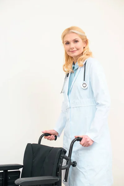 Mature female doctor with wheelchair on white — Stock Photo