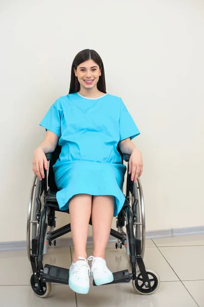 Счастливая беременная женщина в медицинском пальто сидит на инвалидной коляске — стоковое фото
