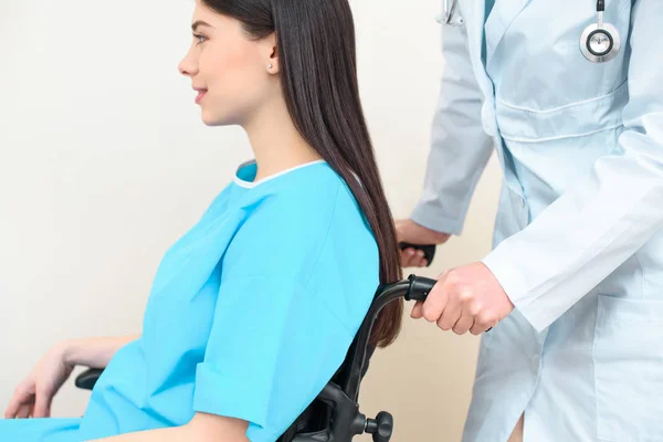 Tiro recortado de ginecólogo obstetra montar mujer embarazada en silla de ruedas en el hospital de maternidad - foto de stock
