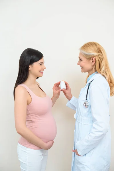 Ginecólogo obstetra y mujer embarazada sosteniendo frasco de píldoras - foto de stock