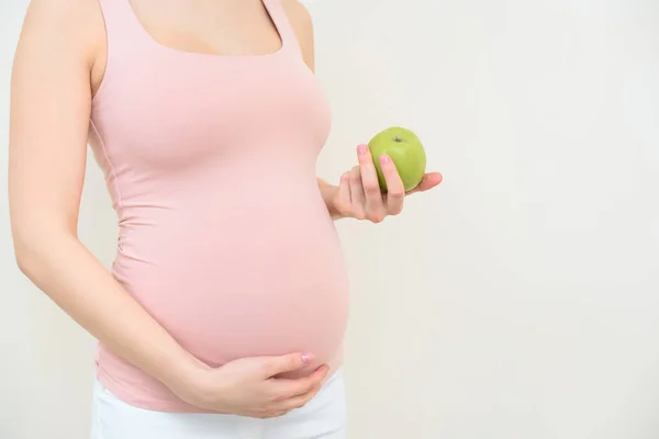 Обрізаний знімок вагітної жінки з зеленим яблуком на білому — стокове фото