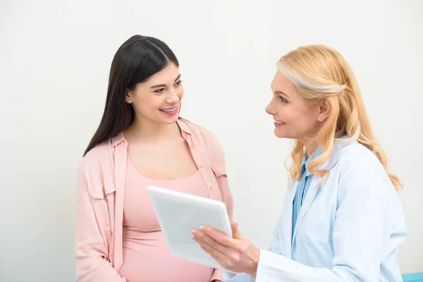 Ginecólogo obstetra madura y mujer embarazada usando tableta juntos - foto de stock