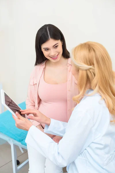 Ginecólogo obstetra y mujer embarazada joven usando tableta juntos - foto de stock