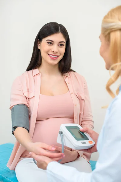 Ginecólogo obstetra medición de la presión arterial de la mujer embarazada sonriente en la clínica - foto de stock