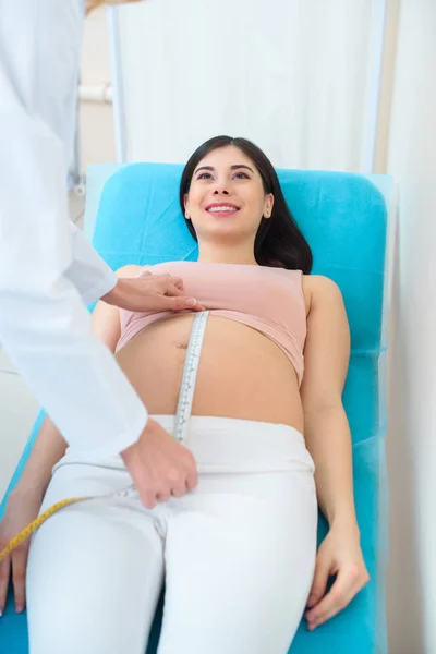 Obstetrician gynecologist measuring belly size of pregnant woman with measuring tape on sofa — Stock Photo