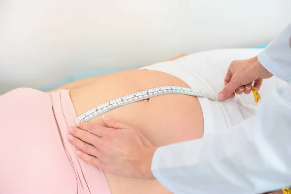 Обрізаний знімок акушера-гінеколога, що вимірює розмір живота вагітної жінки з мірною стрічкою — стокове фото