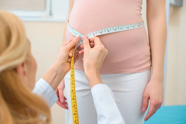 Primer plano de ginecólogo obstetra medición del tamaño del vientre de la mujer embarazada con cinta métrica - foto de stock