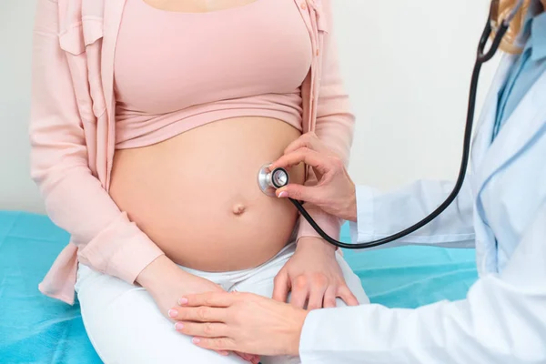 Обрізаний знімок акушер-гінеколога, що слухає серцебиття дитини плоду вагітної жінки зі стетоскопом — стокове фото