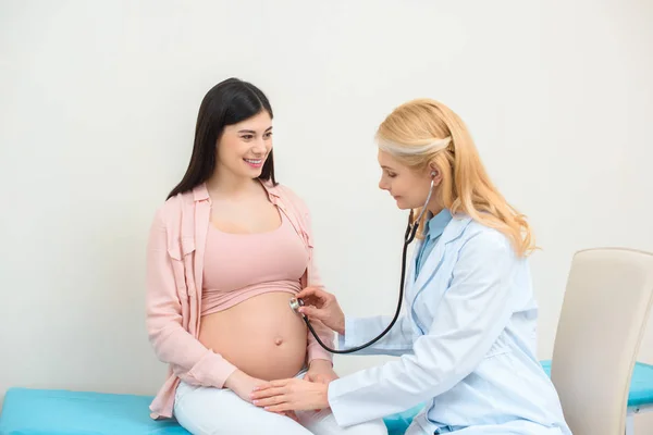 Obstetrician gynecologist listening heartbeat of child fetus of pregnant woman with stethoscope — Stock Photo