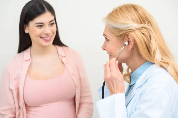 Close-up shot of obstetrician gynecologist listening heartbeat of child fetus of pregnant woman with stethoscope — Stock Photo