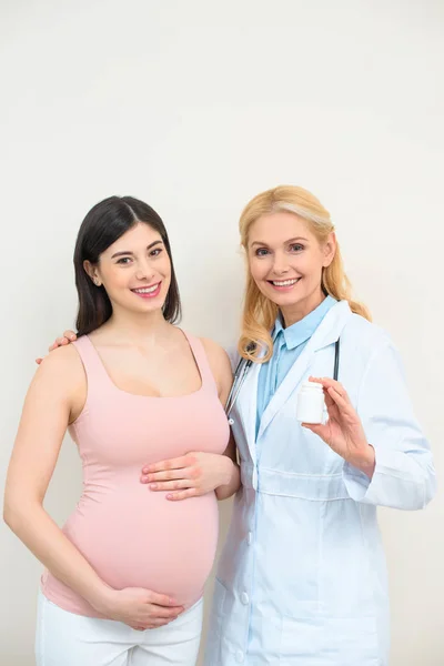 Ginecologista obstetra e mulher grávida com frasco de pílulas olhando para a câmera — Fotografia de Stock