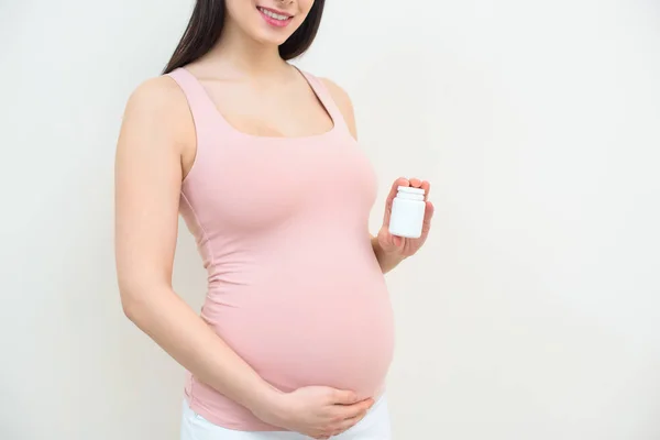 Colpo ritagliato di donna incinta in possesso di vaso di pillole su bianco — Foto stock