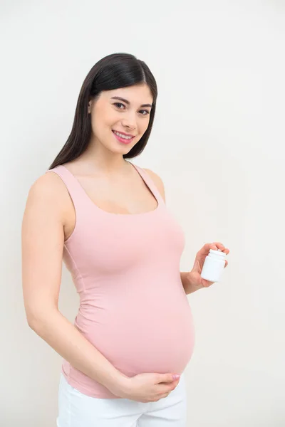 Счастливая молодая беременная женщина держит банку таблеток на белом — стоковое фото