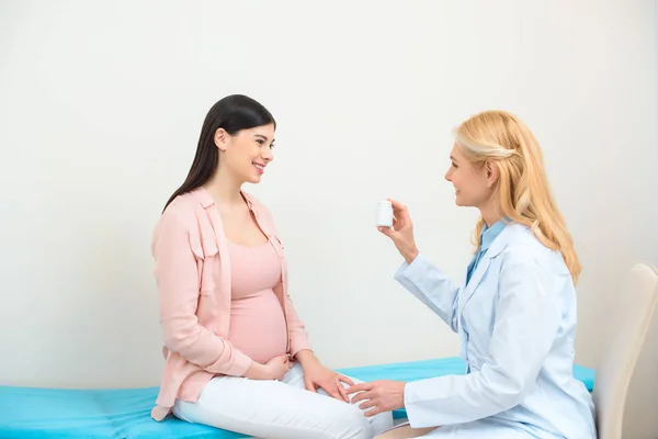 Gynécologue obstétricien montrant pot de pilules à la jeune femme enceinte — Photo de stock