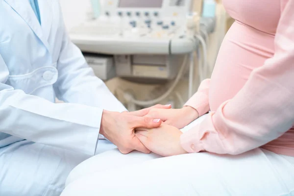 Inyección recortada de ginecólogo obstétrico cogido de la mano de la mujer embarazada - foto de stock