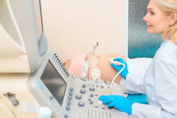 Vista lateral del ginecólogo obstetra haciendo ecografía para la mujer embarazada - foto de stock