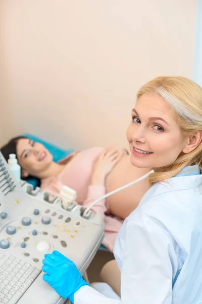Ginecólogo obstetra madura feliz haciendo examen de ultrasonido para la mujer embarazada - foto de stock
