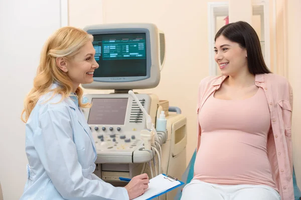 Ginecóloga ginecóloga obstetra femenina madura consultando a una mujer embarazada en la oficina de ultrasonido - foto de stock