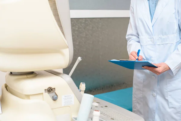 Obstetrician gynecologist in front of ultrasonic scanner writing in clipboard — Stock Photo