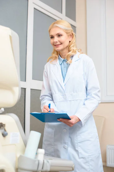 Obstetrician gynecologist looking at ultrasonic scanner and writing in clipboard — Stock Photo