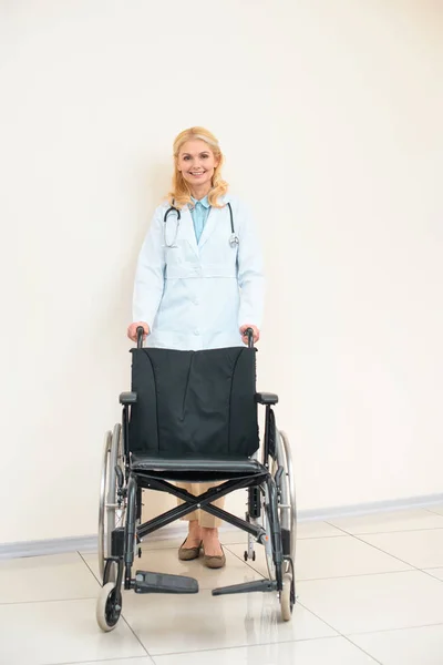 Adulte femme médecin avec fauteuil roulant regardant caméra — Photo de stock