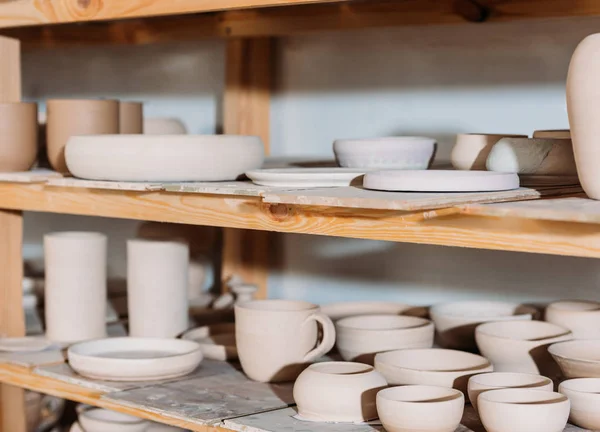 Primer plano de platos de cerámica y cuencos en estantes de madera en taller de cerámica - foto de stock