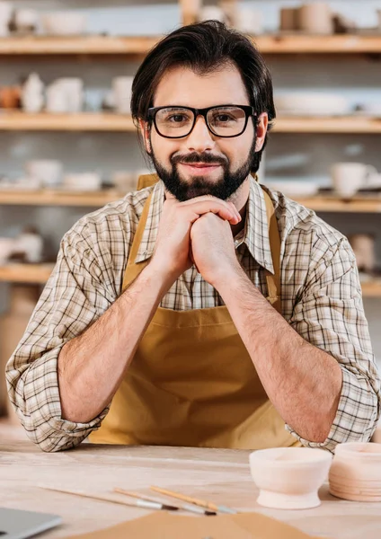 Ritratto di ceramista sorridente in grembiule seduto in laboratorio — Foto stock