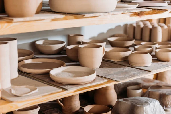 Ceramic plates and bowls on wooden shelves in pottery workshop — Stock Photo