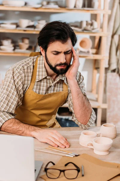 Alfarero macho cansado en delantal sentado en el taller - foto de stock