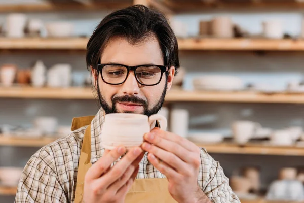 Мужчина гончар глядя на керамическую чашку в мастерской — Stock Photo