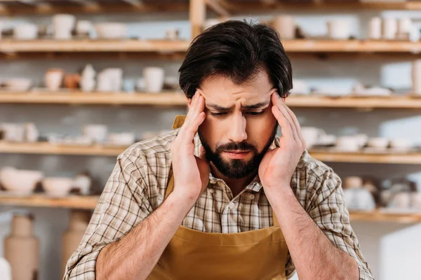 Oleiro masculino cansado tendo dor de cabeça enquanto sentado na oficina — Fotografia de Stock
