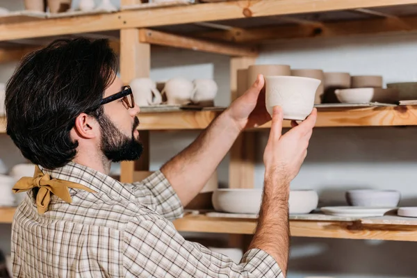 Мужчина гончар с керамической посудой на полках в мастерской — стоковое фото