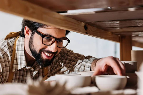 Ceramista sorridente che lavora con stoviglie in ceramica in laboratorio — Foto stock