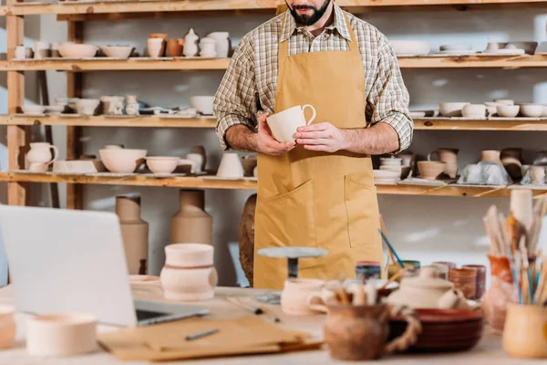 Abgeschnittene Ansicht eines Mannes mit Keramiktasse in Töpferei-Werkstatt — Stockfoto