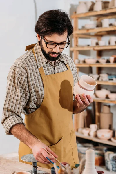 Male potter painting traditional ceramic dishware in workshop — Stock Photo