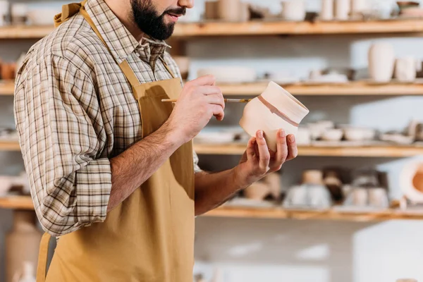 Cropped view of male potter painting ceramic dishware with brush in workshop — Stock Photo