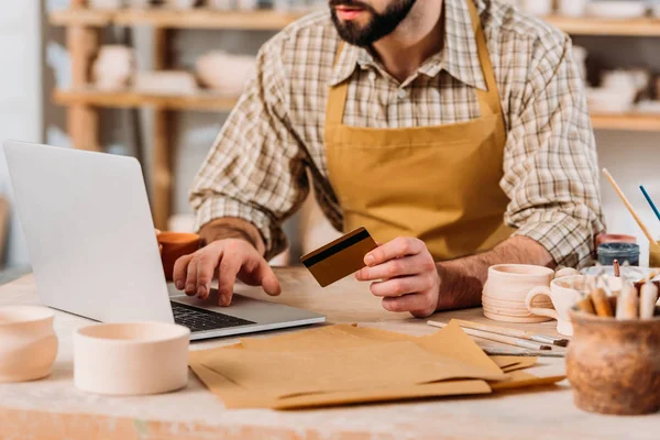Cropped view of potter shopping online with laptop and credit card in workshop — Stock Photo