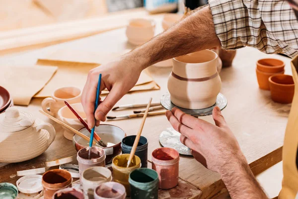 Cropped view of male potter painting ceramic dishware in workshop — Stock Photo