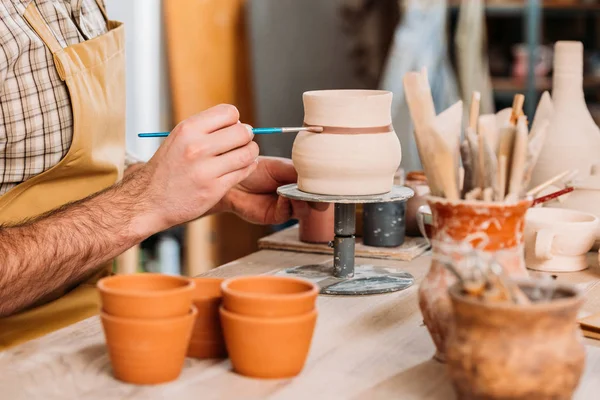 Vue recadrée de pot en céramique de peinture de potier avec pinceau en atelier — Stock Photo