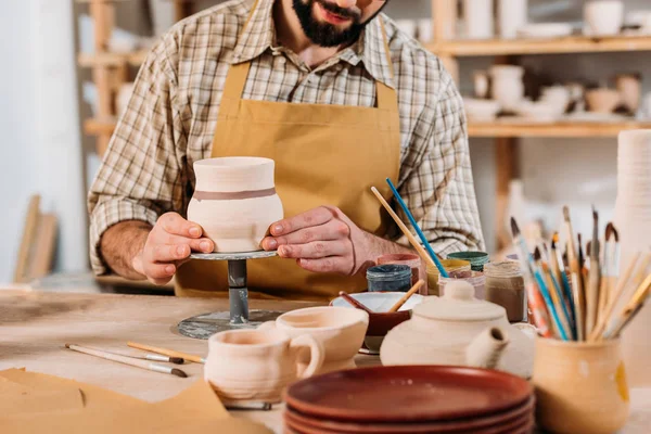 Vue recadrée de l'homme peignant vaisselle en céramique dans l'atelier de poterie — Photo de stock