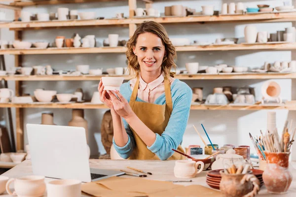 Beautiful potter with ceramics and laptop in workshop — Stock Photo