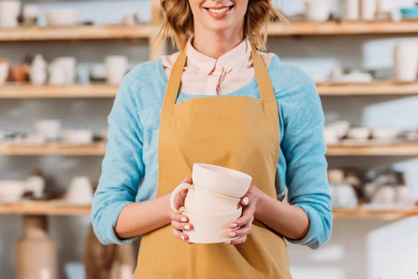 Cropped view of potter in apron holding ceramic bowls — Stock Photo