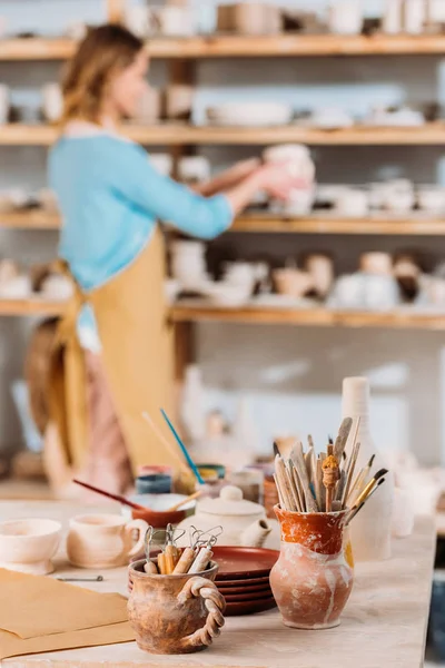 Foyer sélectif de potier en atelier avec céramique et pinceaux au premier plan — Photo de stock